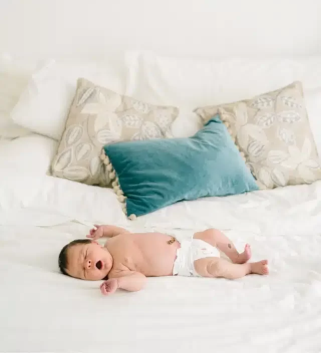 a newborn laying on a bed with 3 pillows