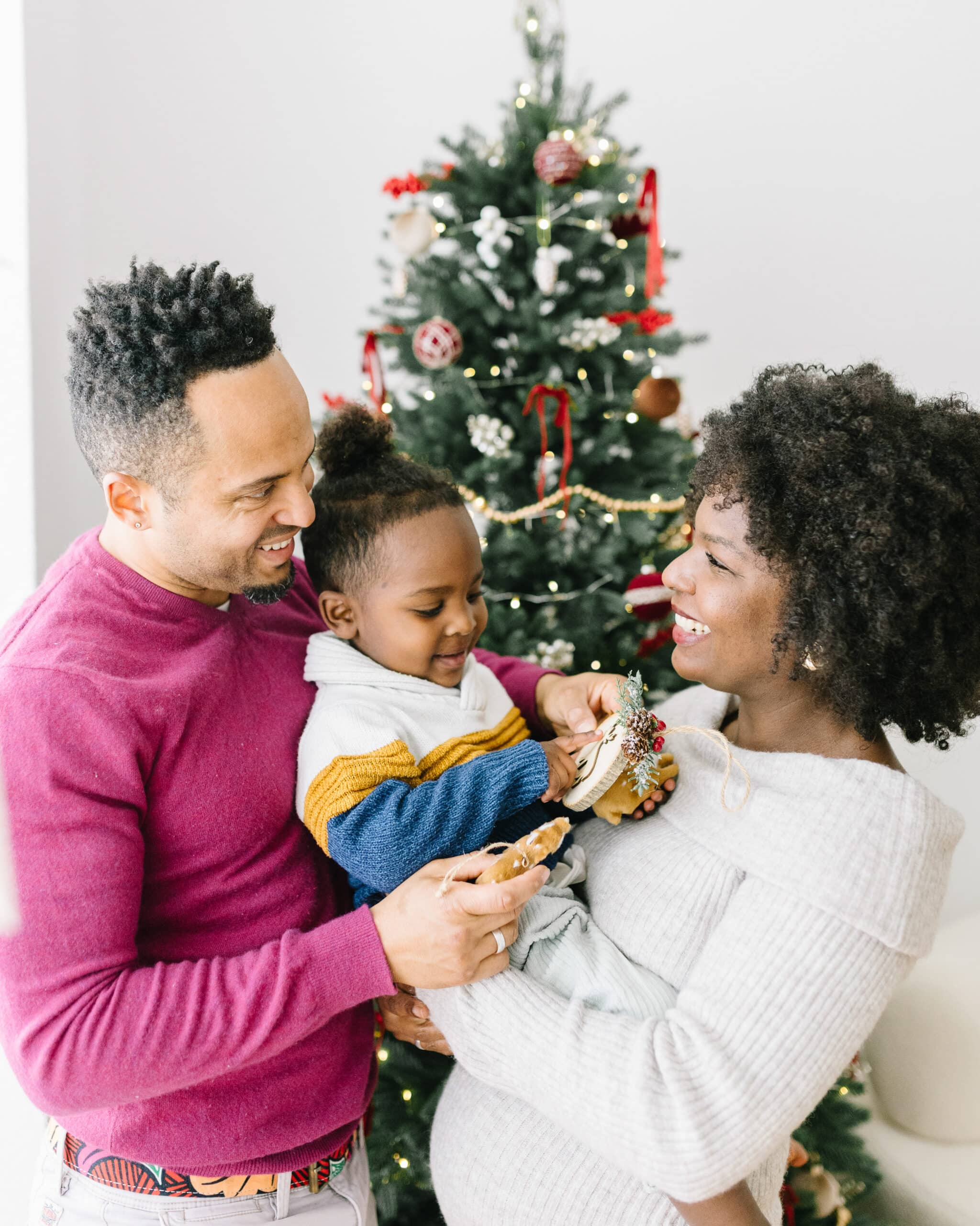 Eltern lachen gemeinsam mit ihrem kleinen Kind vor einem geschmückten Weihnachtsbaum im Fotostudio in Bonn.