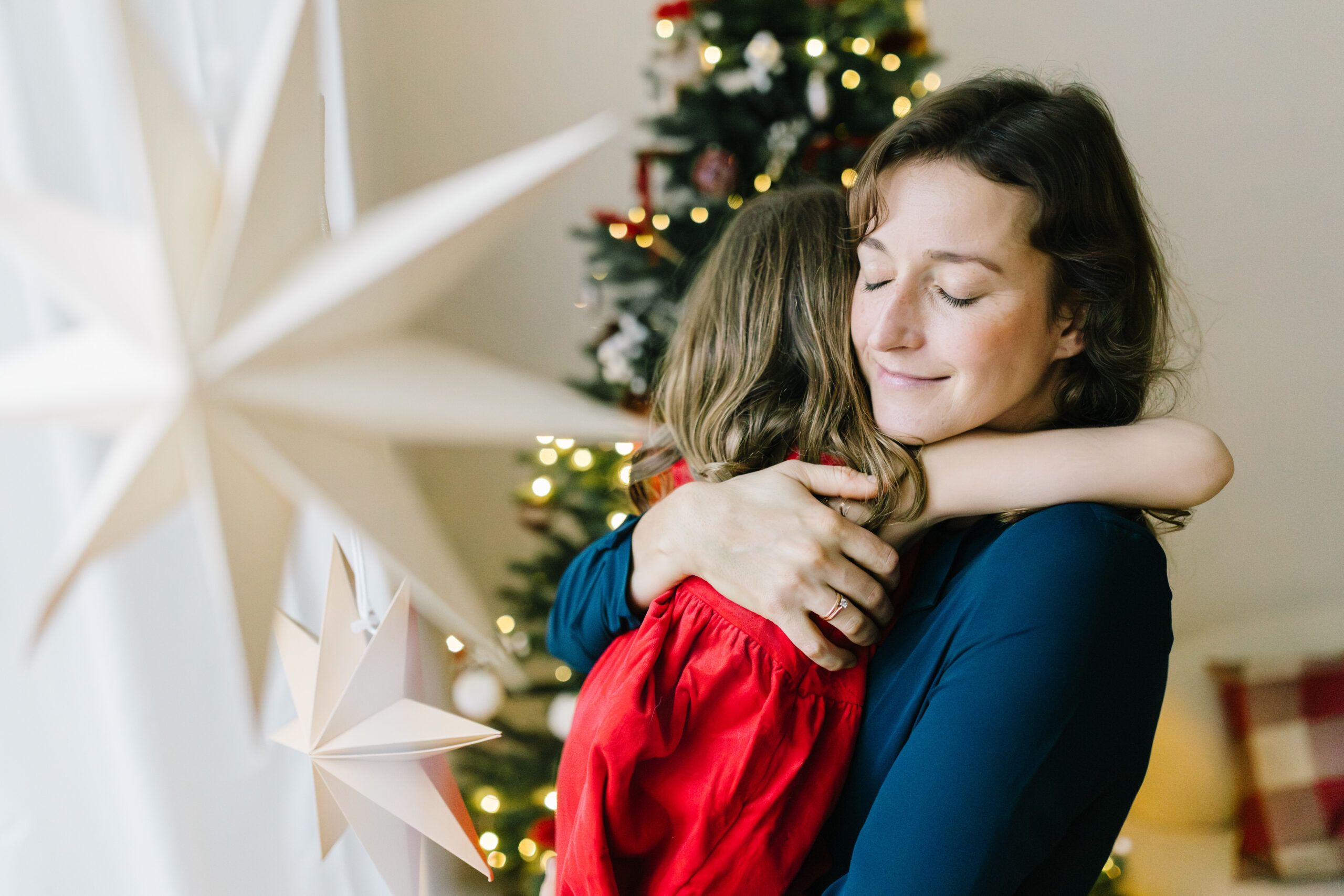Mutter umarmt ihre Tochter liebevoll vor einem beleuchteten Weihnachtsbaum beim Weihnachtsshooting in Bonn.