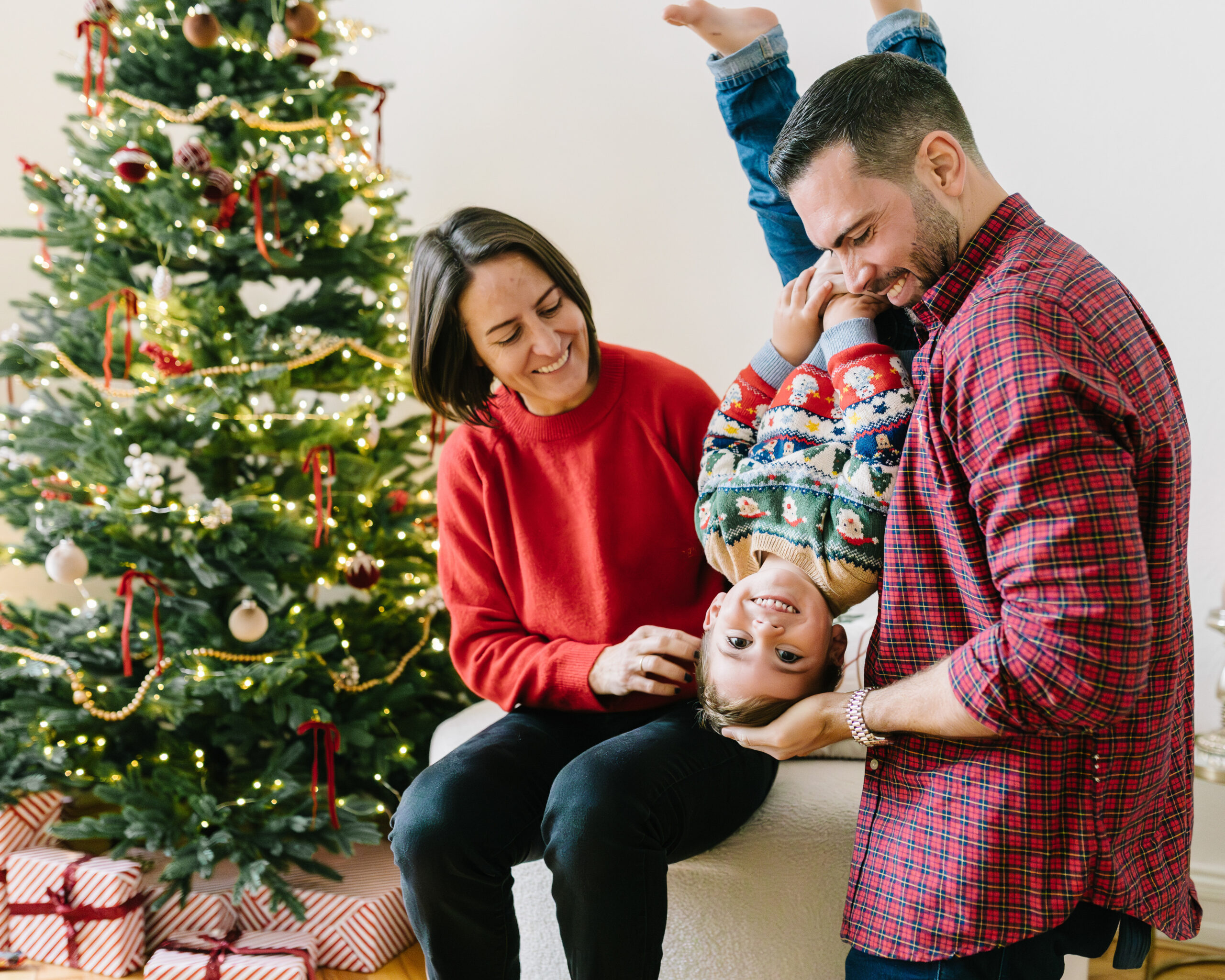 Eltern spielen ausgelassen mit ihrem Sohn neben einem festlich geschmückten Weihnachtsbaum.