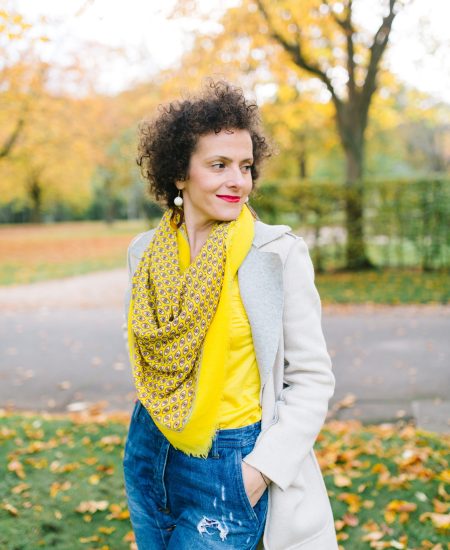 Curly-haired woman wearing a yellow top and blue jeans standing in a park in Bonn, Germany